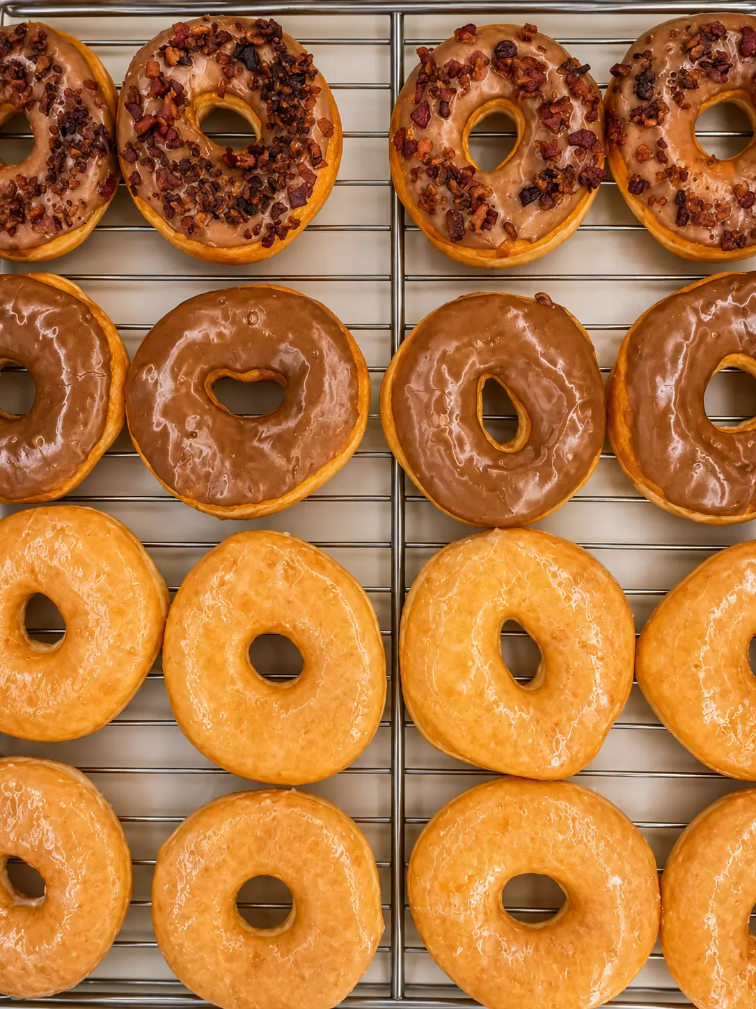 Glazed ring donuts and irregular apple fritters on a bakery rack at Atlanta Donuts.